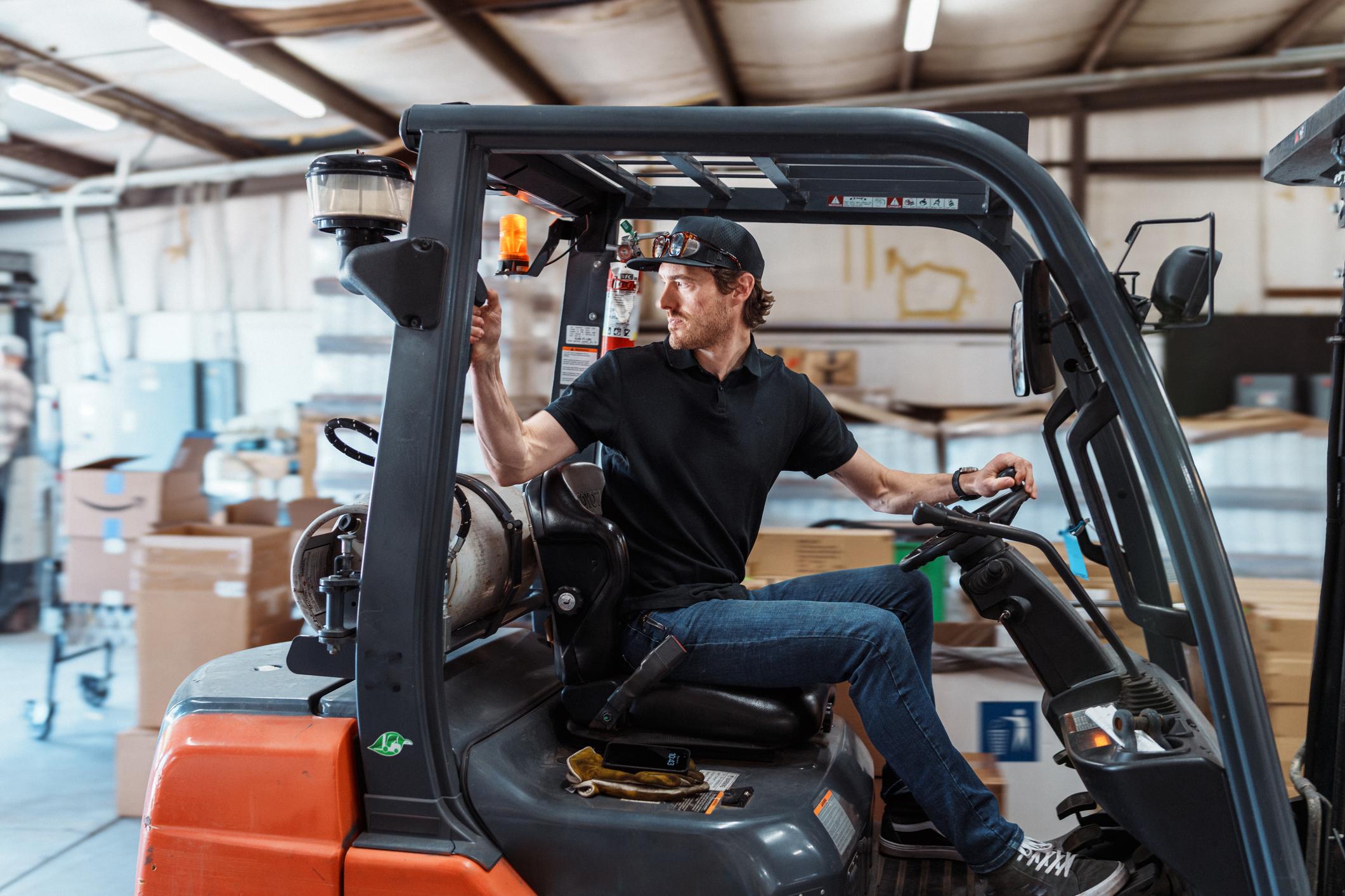 A man operates a forklift in reverse when working in a manufacturing and fabrication facility.